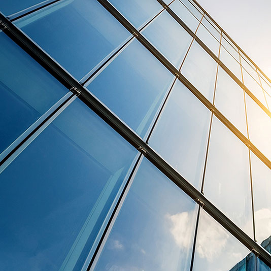 A low-angle view of a modern glass building reflecting the sky and sunlight.