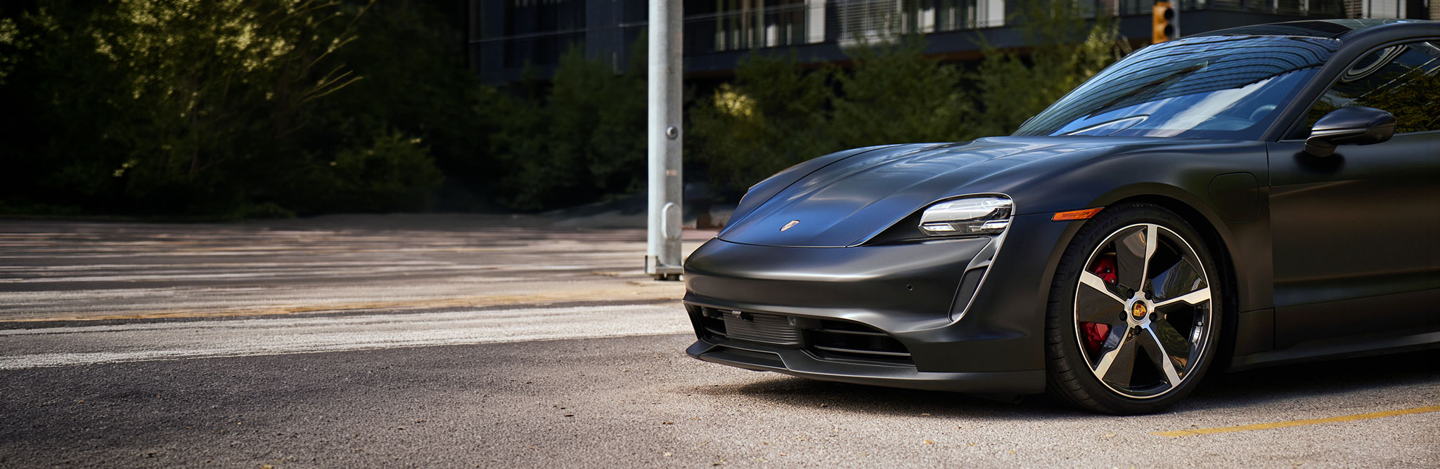 A matte black Porsche Taycan electric sports car parked on a city street 